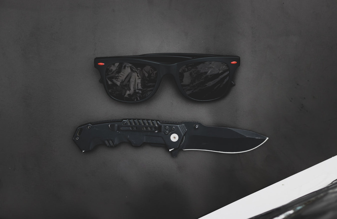 Tactical Equipment which includes black military knife and sunglasses. 